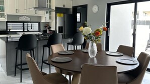 A modern kitchen with a central island, a dining area with a round table and chairs, and a view through a glass door.