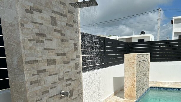 A shower area with a stone wall and a pool in the background.