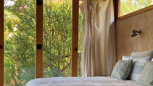 Ein Schlafzimmer mit einem Bett, einem Fenster mit Vorhängen und Blick auf Grünfläche.