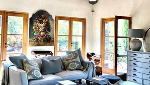 Ein gemütliches Wohnzimmer mit hoher Holzbalkendecke, einem hellblauen Sofa, einem dunkelblauen Hocker und einem weißen, flauschigen Teppich.