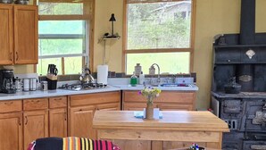 A kitchen with wooden cabinets, a gas stove, a sink, and a stove with a chimney. - Our Little Cabin, Life As It Should Be (Philipsburg)