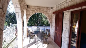 A covered patio with stone walls, a table with chairs, and a view of greenery. - Apartment Nemo - Three Bedroom Apartment with Terrace (Njivice)
