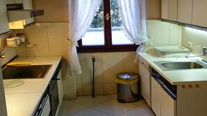 A compact kitchen with white cabinets, a sink, a stove, and a window with curtains. - Apartment Nemo - Three Bedroom Apartment with Terrace (Njivice)