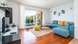 A modern living room with a sofa, a coffee table, and a TV. There is a sliding glass door leading to an outdoor area with chairs and a table. - Apartment Doma - Two Bedroom Apartment with Terrace (Cavtat)