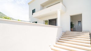 A modern building with a white exterior, a set of beige steps leading to a door, and a small balcony with a potted plant. - Apartment Doma - Two Bedroom Apartment with Terrace (Cavtat)