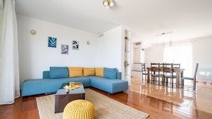 A modern living room with a blue sofa, wooden dining table, and a yellow pouf. - Apartment Doma - Two Bedroom Apartment with Terrace (Cavtat)