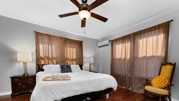 Une chambre à coucher comprenant un lit, des tables de chevet, une chaise, un ventilateur de plafond et des rideaux.