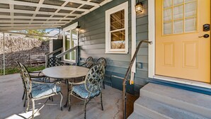 Une terrasse couverte avec une table et des chaises, une porte jaune et un escalier menant à la maison.