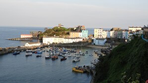 A coastal town with a harbor filled with boats, colorful buildings, and a prominent hill with a structure on top. - Former Coach House in quiet hamlet in Pembrokeshire (Neyland)