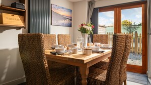 A dining area with wicker chairs, a wooden table, and a painting on the wall. - Former Coach House in quiet hamlet in Pembrokeshire (Neyland)