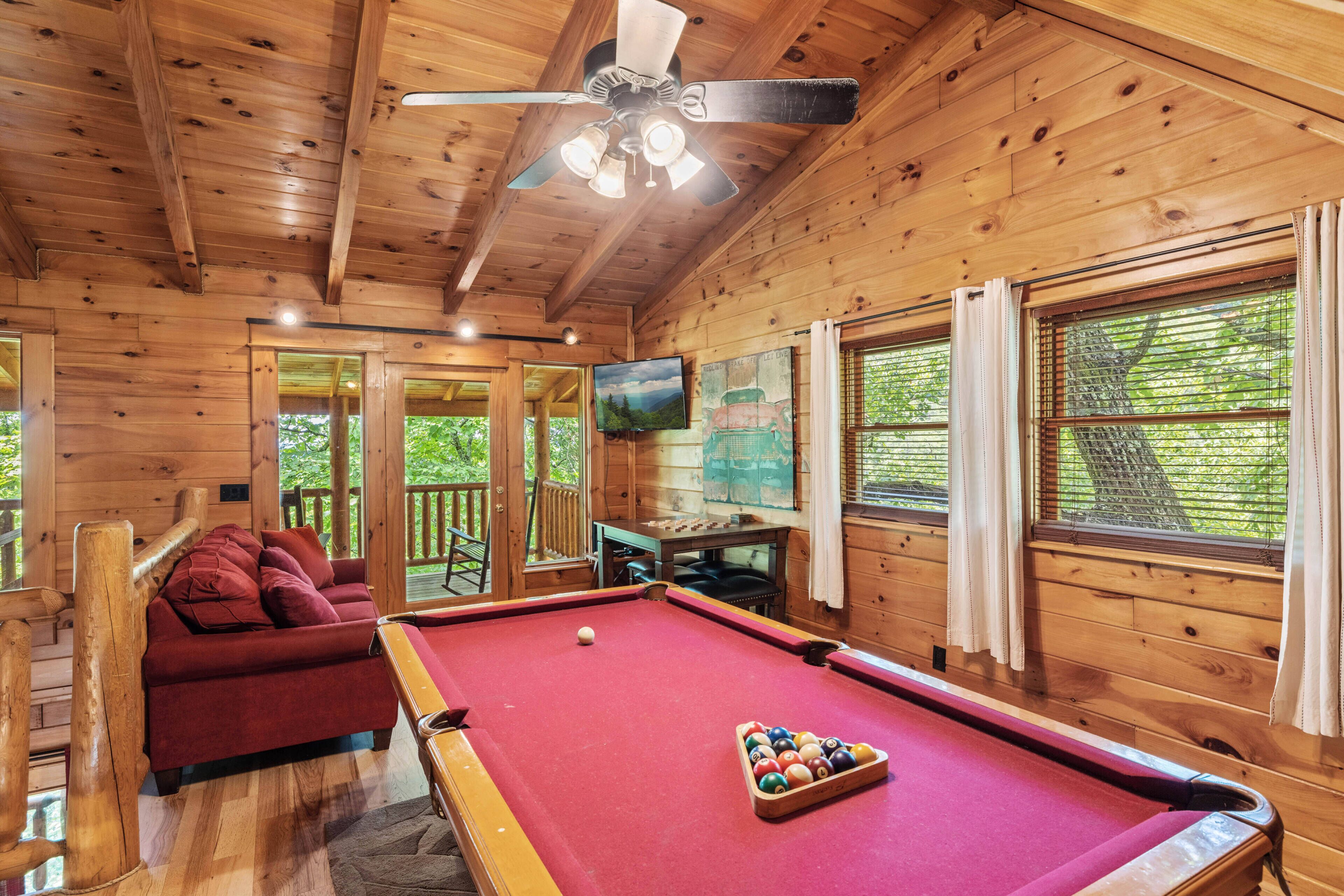 A wooden cabin with a pool table, a red sofa, and a ceiling fan.