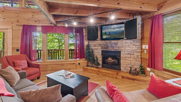 Interior acogedor de una cabaña con chimenea de piedra, muebles de madera y ventanas amplias.