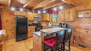Cocina tipo cabaña de madera con refrigerador, microondas, estufa y armarios de madera.