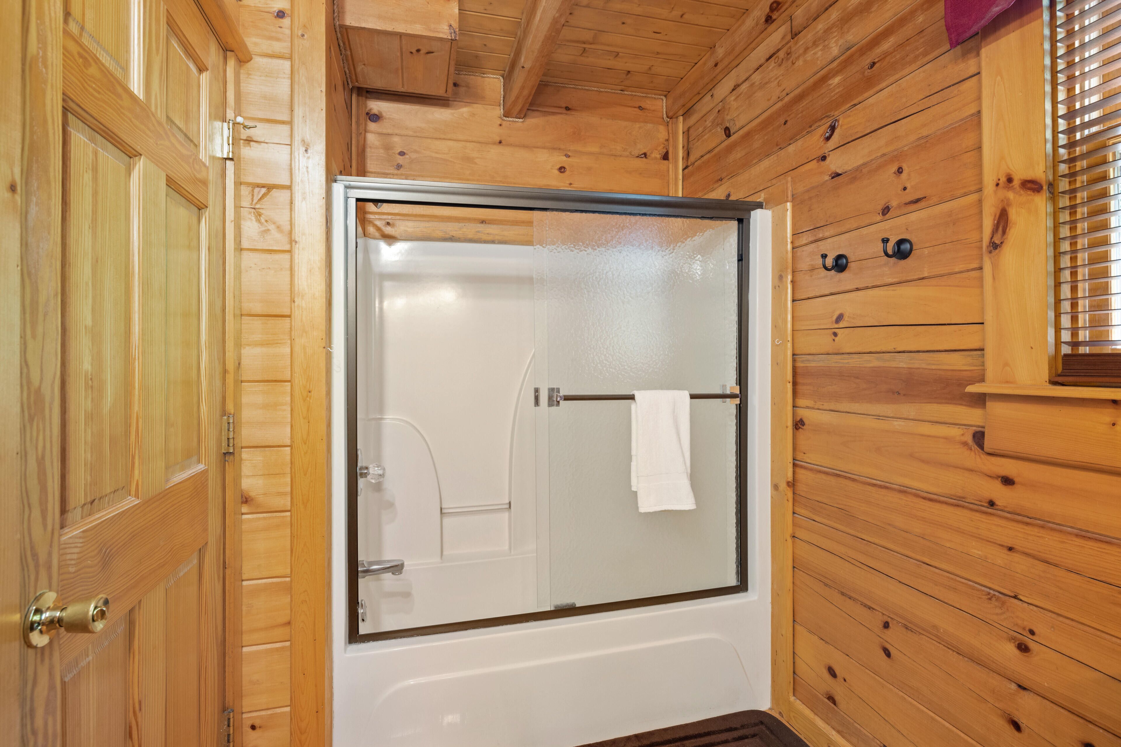 Ein Badezimmer einer Holzhütte mit einer Duschkabine aus Glas, einer weißen Badewanne und einem Handtuch an einem Handtuchhalter.