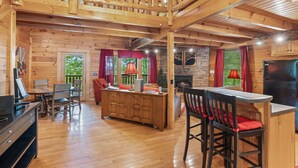 Interior de una cabaña de madera con comedor, cocina y chimenea.