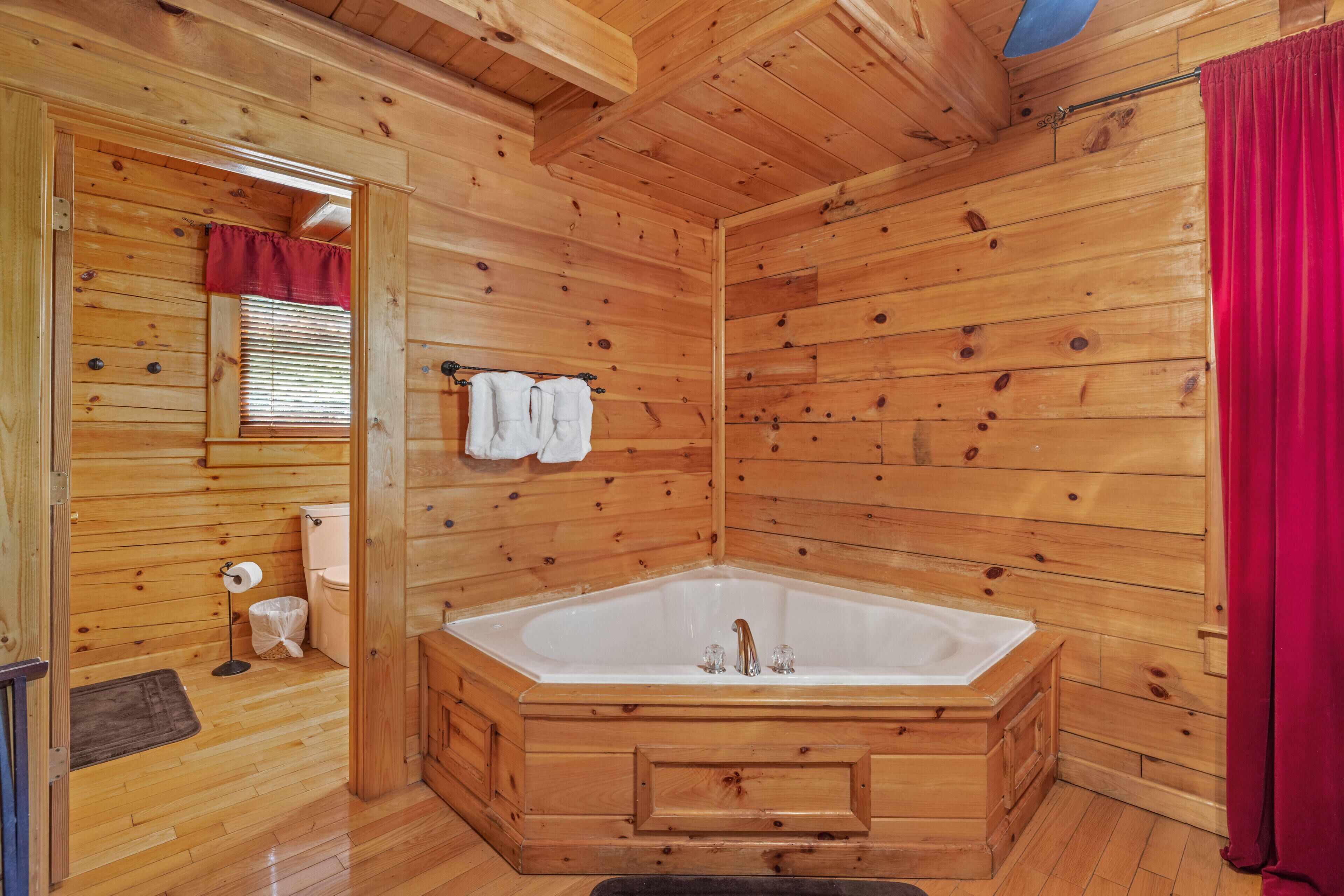 A wooden cabin bathroom with a large bathtub, wooden walls, and a red curtain.