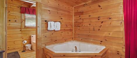 A wooden cabin bathroom with a large bathtub, wooden walls, and a red curtain.