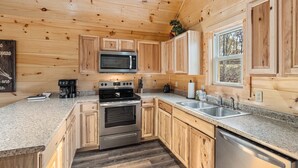 A modern kitchen with wooden cabinets, stainless steel appliances, granite countertops, and a window providing natural light.