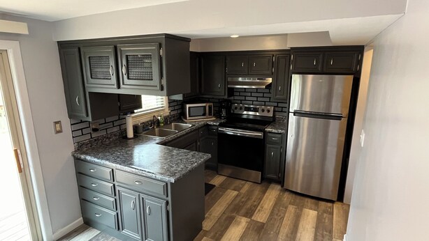 A modern kitchen with dark cabinetry, a stainless steel refrigerator, a microwave, and a stove. - Walk to Lambeau, Resch, Expo, and Titletown (Green Bay)
