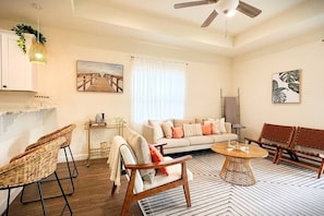 Un salon spacieux comprenant un canapé, deux fauteuils en bois, une table basse et un ventilateur de plafond.