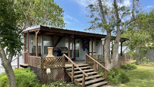 Une cabane rustique dotée d’une terrasse en bois, d’une cheminée et d’un barbecue à l’extérieur.