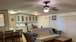Un espace de vie compact comprenant un coin repas, une kitchenette et un canapé agrémenté d’une commode en bois.