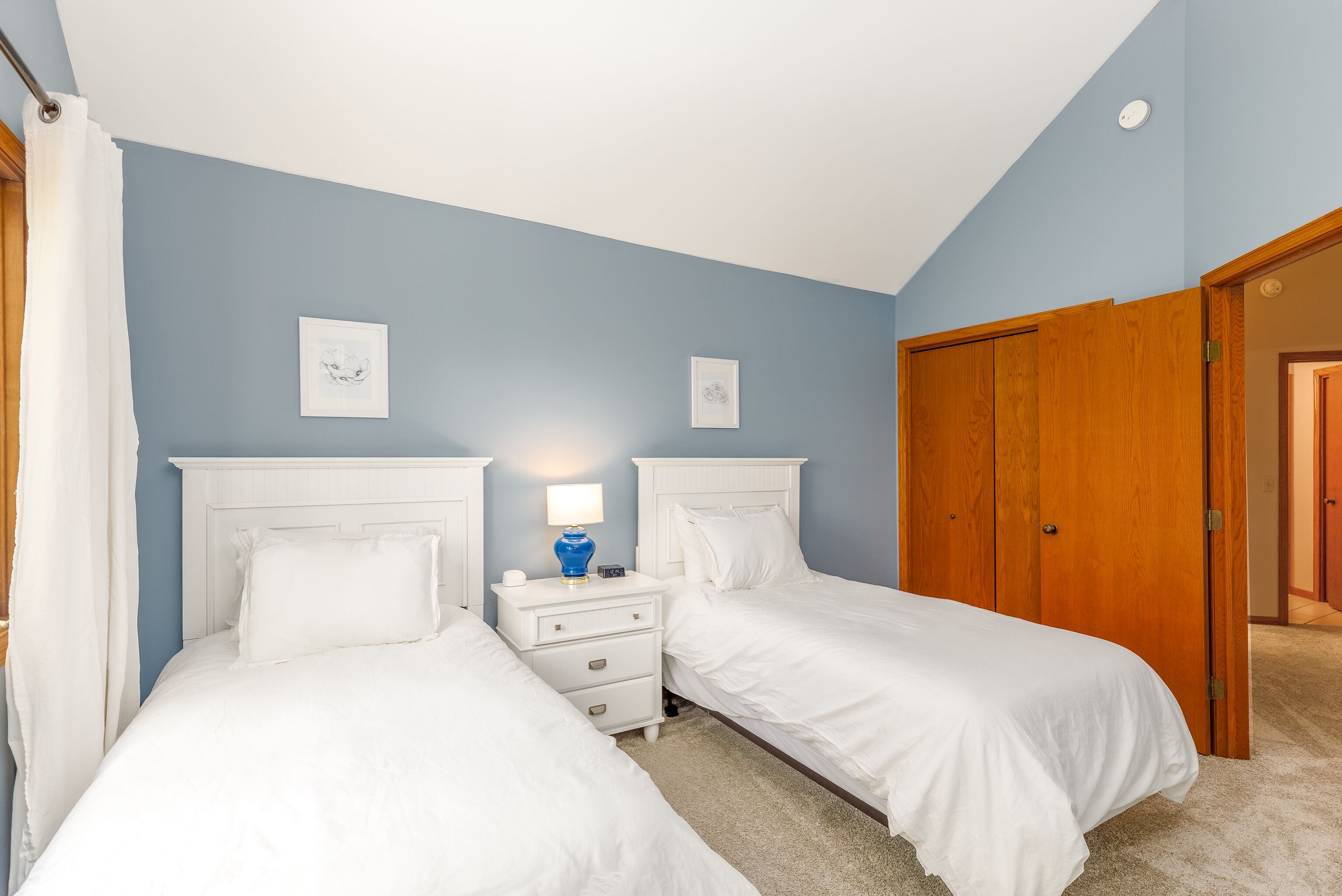 Een slaapkamer met twee eenpersoonsbedden, een nachtkastje met een lamp en een houten garderobe.