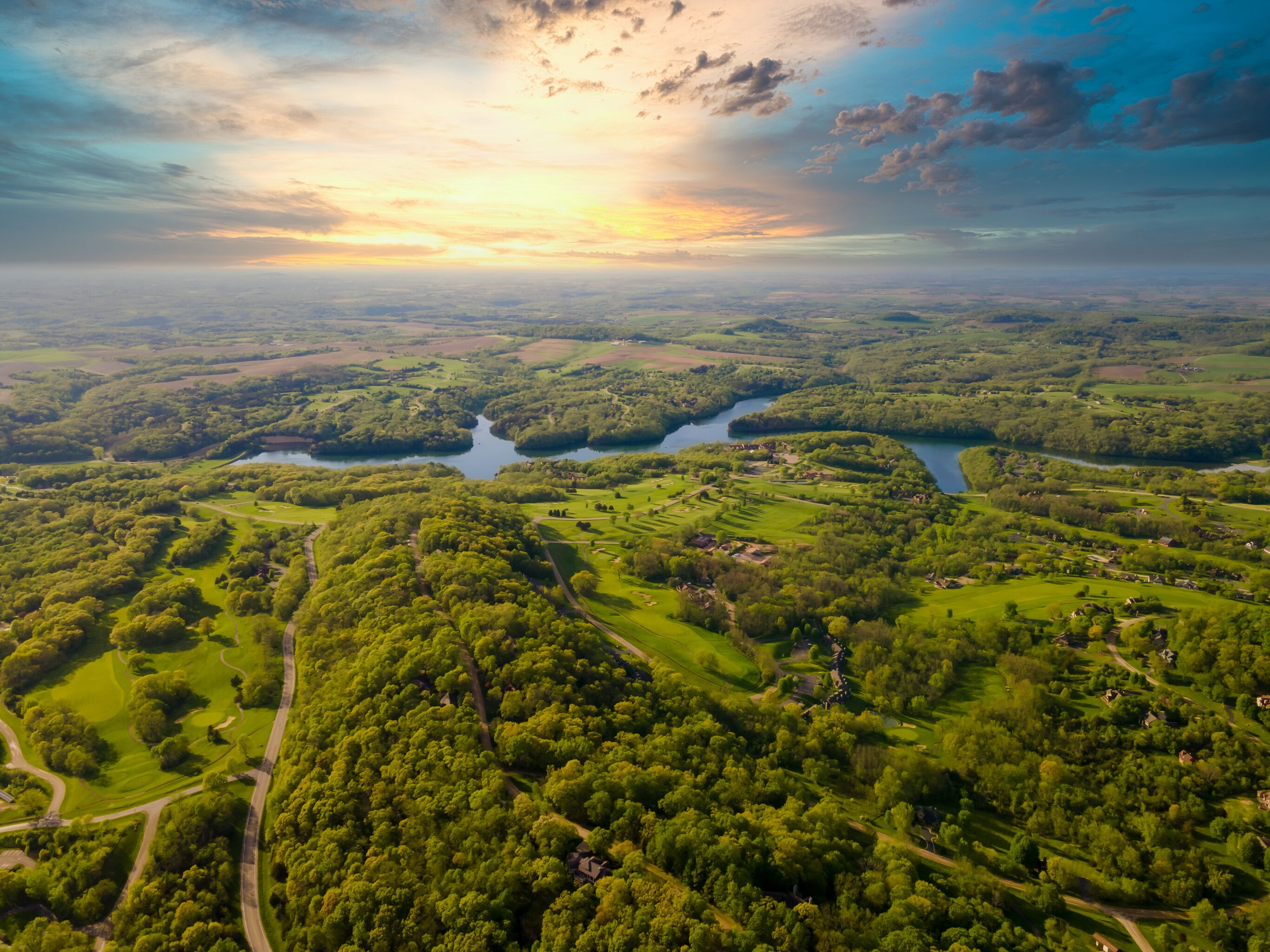 An aerial view of a lush landscape with a river, green fields, and scattered buildings.