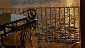 Un balcón con mesa y sillas, con vista a una masa de agua al atardecer.