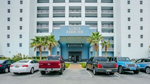 Un estacionamiento con varios vehículos, incluyendo un sedán blanco, una camioneta roja y un SUV azul, frente a un edificio con un letrero que dice 'South Harbour'.