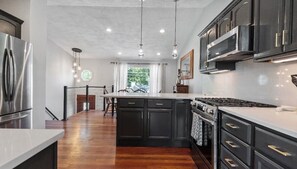 Una cocina moderna con una isla central, muebles oscuros, electrodomésticos de acero inoxidable e iluminación colgante.