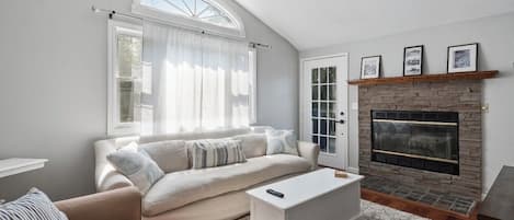 A living room with a sofa, a fireplace, a window with curtains, and a door.