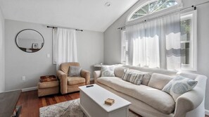 A living room with a sofa, armchair, coffee table, and a round mirror on the wall.