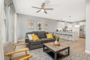 A modern living room with a grey sofa, yellow cushions, a wooden coffee table, and a ceiling fan.