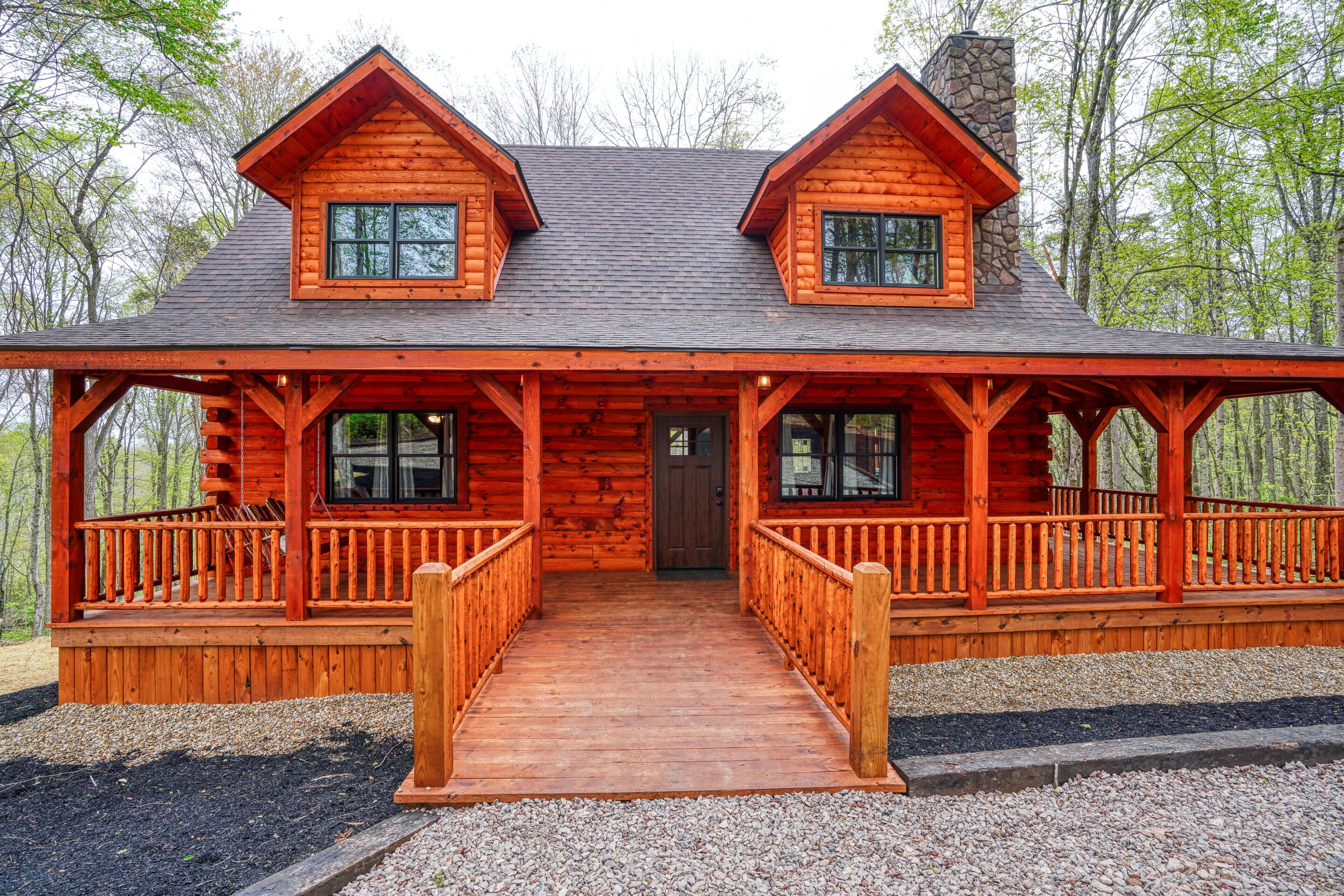 A log cabin with a front porch, two windows, and a stone chimney.