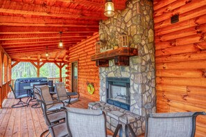 A log cabin with a stone fireplace, outdoor seating, and a barbecue grill.