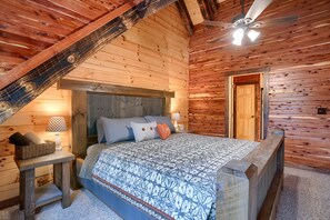 A wooden cabin bedroom with a bed, a nightstand, a lamp, and a ceiling fan.