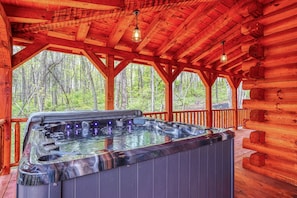 A wooden cabin with a hot tub and a view of the forest.