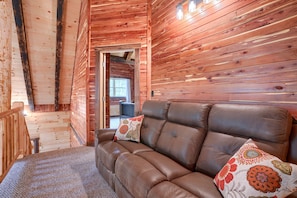 A wooden cabin interior with a leather sofa, wooden walls, and a visible door leading to another room.
