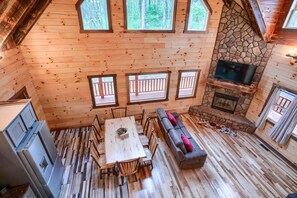 A wooden cabin interior with a dining area, sofa, stone fireplace, and a television.