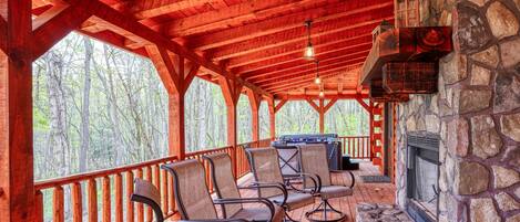A covered outdoor seating area with wooden chairs and a stone fireplace.