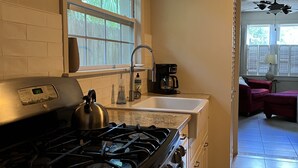 Une cuisine équipée d’une cuisinière à gaz, d’une machine à café et d’une fenêtre avec des stores.