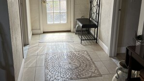 Un couloir avec un sol carrelé, un banc, une porte avec une fenêtre et un vase décoratif.