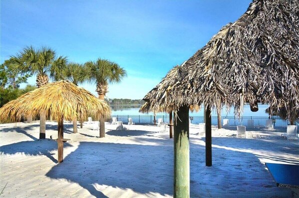 A beach with thatched umbrellas, palm trees, and lounge chairs.