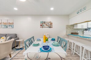 A dining area with a white table set with blue and white plates, surrounded by white chairs. - Modern~ Ground floor Condo~ 4 mins walk to Beach! Sleeps 6 (Fort Walton Beach)