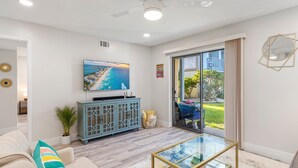 A modern living room with a flat-screen TV, a glass coffee table, and a view of the outdoors.