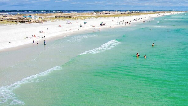 A beach with clear turquoise water, sandy shore, and a long stretch of beach with people and umbrellas.