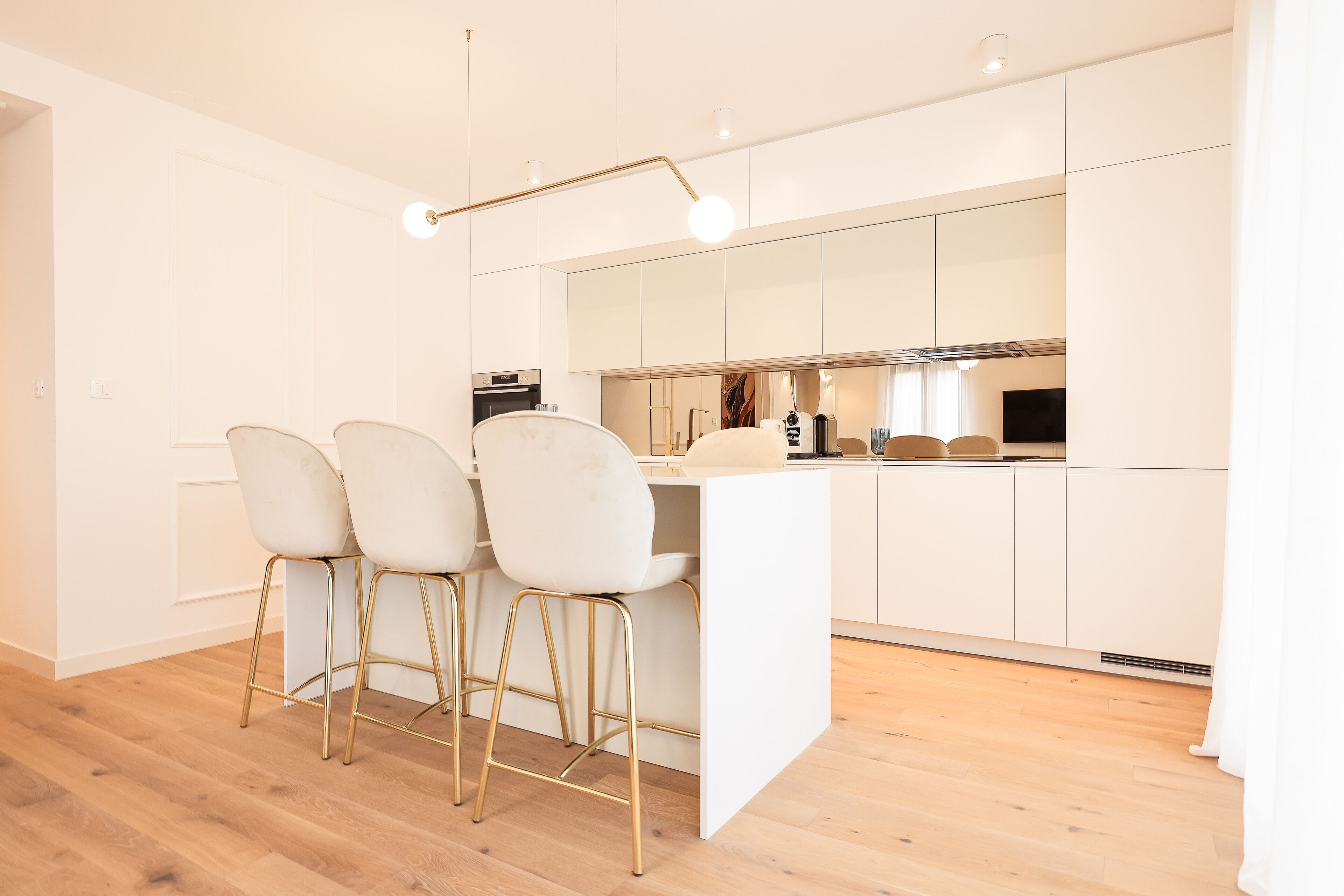Une cuisine moderne avec des meubles blancs, un îlot central et trois tabourets de bar aux pieds dorés.