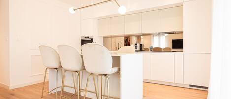Une cuisine moderne avec des meubles blancs, un îlot central et trois tabourets de bar aux pieds dorés.