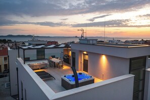 A rooftop terrace with a hot tub, outdoor seating, and a view of the sea at sunset. - Adria Concept boutique apartments (Zadar)